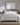 Modern bedroom featuring a neatly styled bed with soft grey SFERRA bedding, set against a white brick wall with warm lighting, natural wood accents, and minimalist decor.